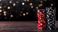 Stacks of red and black poker chips on dark wooden table against blurred golden bokeh lights background, casino gaming concept.