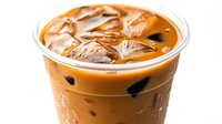 Refreshing iced coffee drink with milk in plastic cup, condensation droplets on surface, ice cubes floating on creamy brown liquid against white background.