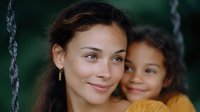 Young Hispanic mother and mixed race daughter on swing set share tender moment outdoors, expressing joy and connection in natural setting with soft bokeh background.