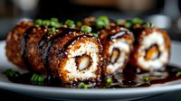 Crispy fried sushi rolls with creamy filling, glazed in rich teriyaki sauce, topped with sesame seeds and green onions on a plate.