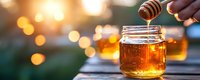 Golden honey dripping from wooden dipper into glass jar at sunset, with soft bokeh lights creating warm atmospheric background. Fresh organic sweetness.