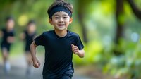 Young Asian boy in black t-shirt and headband running outdoors with joyful expression against blurred green nature background, capturing active lifestyle and childhood energy.