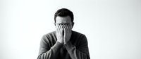 Young Caucasian man covering face with hands expressing stress, depression or shame in monochrome portrait isolated on white background for mental health concepts.