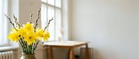 Yellow daffodils and willow branches in a vase on a table by a bright window in a cozy minimalist room, spring home decor.