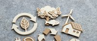 Wooden laser cut eco-friendly symbols including recycling arrows, butterflies, house, and leaf shapes on gray felt background for sustainable design projects.