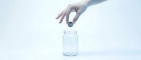 Hand dropping coin into empty glass jar against white background, savings and financial planning concept for investment and money accumulation.