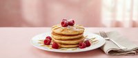 Stack of golden fluffy pancakes topped with fresh raspberries on white plate with fork and napkin, breakfast food concept for restaurant menu design.