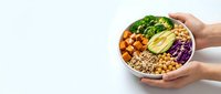 Hands holding nutritious bowl with roasted vegetables, grains, leafy greens and legumes for healthy eating and meal prep.