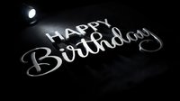 Happy Birthday text in silver metallic lettering on dark background with spotlight illumination, suitable for greeting cards, invitations, and celebration designs.