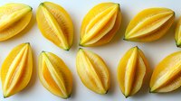 Fresh ripe yellow starfruit slices arranged in rows on white background, showing juicy tropical carambola segments with distinctive ridged pattern.