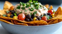 Loaded nachos with black beans, corn, tomatoes, sour cream and fresh cilantro served in bowl. Mexican appetizer ready for party or game day celebration.