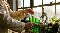 Scientist conducting plant research experiment with green test tubes in modern laboratory greenhouse for botanical studies and agricultural development.