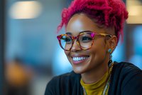 Young African American woman with vibrant pink hair and stylish glasses smiling warmly against blurred background. Natural genuine expression shows joy and confidence.