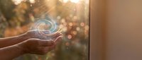 Hands holding glowing spiral light orb against warm sunset window backdrop with bokeh effect, representing energy, innovation, and future technology concepts.