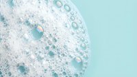 Foamy soap bubbles and lather texture on mint green background for skincare, bath products, cleaning supplies and hygiene concepts.