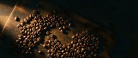 Roasted coffee beans arranged in heart shape on rustic wooden surface with warm lighting for cafe branding and beverage marketing materials.