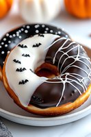 Halloween themed donut decorated with black and white chocolate, featuring spooky bat designs and spider web pattern on white ceramic plate, seasonal treat.