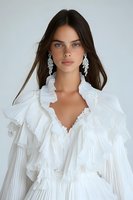 Young woman with long dark hair wearing white ruffled romantic dress and crystal chandelier earrings against light background. Fashion portrait with soft natural makeup.