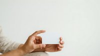 Two hands holding blank business card or small rectangular object against neutral background, suitable for corporate branding and marketing materials.