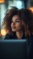 Young African American woman with natural curly hair gazing thoughtfully into distance against blurred bokeh lights, wearing dark sparkly outfit. Professional portrait.