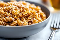 Rotini pasta with rich tomato sauce and parmesan cheese served in gray ceramic bowl on light background, selective focus on twisted noodles, close-up view.