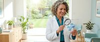 Middle-aged African American female doctor examining medical chart with magnifying glass in bright modern clinic office with plants and natural lighting.