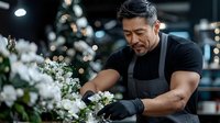 Professional Asian male florist arranging white flowers in modern shop with bokeh lights. Skilled craftsman creating floral arrangements for events and celebrations.