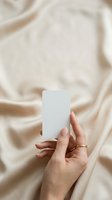 Cropped view of woman's hand holding blank white card against draped beige fabric background, suitable for branding, business card mockups, and product presentation designs.