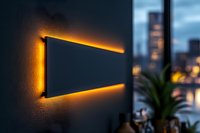 Modern black wall panel illuminated with warm orange LED backlight against blurred urban cityscape background, creating ambient mood lighting effect.