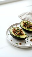 Avocado halves filled with seasoned ground meat and fresh herbs served on white plate for healthy lunch or dinner meal preparation.