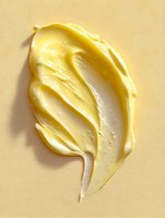 Creamy yellow butter smear with textured swirl pattern on light beige background, showing smooth glossy surface and rich dairy consistency for food design.