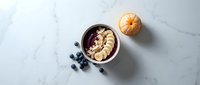Acai bowl with granola and blueberries on marble surface, overhead view. Healthy breakfast and smoothie bowl concept for food and wellness design.