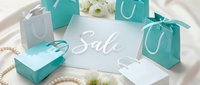 Elegant turquoise and white gift bags with pearl necklace and flowers surrounding a sale sign on silk fabric for luxury retail promotion.
