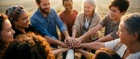 Diverse group of people joining hands together in team building circle outdoors during golden hour sunset creating unity and connection moment.
