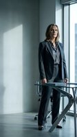 Confident mature businesswoman in dark suit standing by office window with natural light, professional corporate executive portrait for business content.
