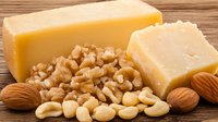 Fresh yellow cheese block with assorted raw nuts including cashews, walnuts and almonds on rustic wooden background, macro food photography for menu design.