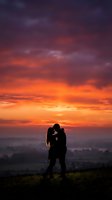 Romantic couple silhouette embracing against dramatic sunset sky with vibrant orange and purple clouds over landscape for love and relationship concepts.