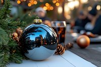 Blue Christmas ornament ball reflecting city skyline with evergreen branches and warm bokeh lights creating festive holiday atmosphere for seasonal decorations.