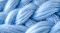Soft blue yarn in macro view showing detailed texture of woven wool threads. Natural fiber material close-up reveals intricate braided pattern and gentle curves.