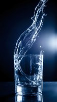 Water splashing into clear glass against dark blue background, dynamic liquid motion with droplets and waves, suitable for beverage, health, wellness and hydration marketing materials.