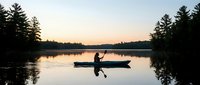 Silhouette of kayaker paddling on calm lake at sunset with forest reflection, peaceful outdoor recreation and water sports adventure.