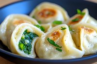Homemade dumplings filled with spinach and herbs served on dark plate, close up view of traditional Asian cuisine with garnish and seasoning.