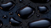 Large black water drops on dark surface with small droplets scattered around creating dramatic contrast and reflection. Golden light adds mysterious glow.