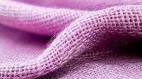 Pink woven fabric with soft waves and textural detail in macro photography, showing natural burlap or linen material fibers in gentle folds.