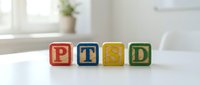 Colorful wooden alphabet blocks spelling PTSD arranged on white surface with bright window background, representing mental health awareness and psychological disorder education.