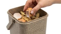 Hand placing eggshell into a compost bin filled with vegetable peels, promoting sustainable waste management and eco-friendly kitchen habits.