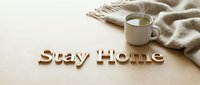 Cozy stay home concept with wooden letters, steaming mug of tea, and soft knit scarf on a warm wooden surface, perfect for lifestyle blogs.