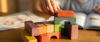 Child playing with colorful wooden building blocks on table, developing creativity and motor skills through educational toy construction activity.