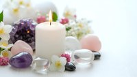 Spa wellness setup with lit candle, healing crystals, gemstones and fresh flowers on white background for relaxation and meditation practices.