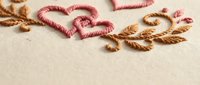 Embroidered heart and floral motifs in pink and brown thread on cream fabric background for romantic crafting and textile design projects.